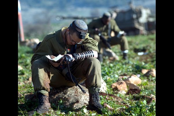 Soldiers praying on the Golan, with their Artillery tank behind them. 