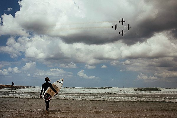 Surfer braves the cold, wind and rain as Israel Air Force jets fly over the Tel Aviv beaches.